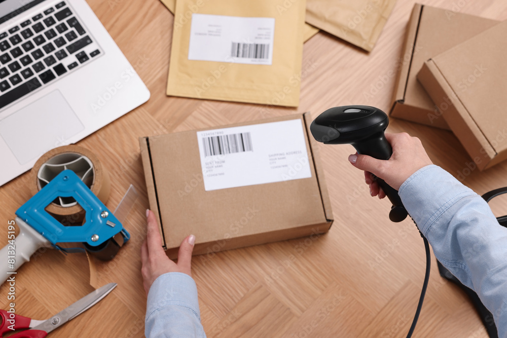 Sticker Parcel packing. Post office worker with scanner reading barcode at wooden table, top view