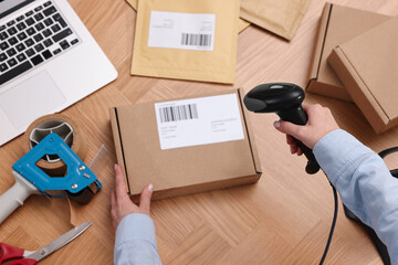 Parcel packing. Post office worker with scanner reading barcode at wooden table, top view