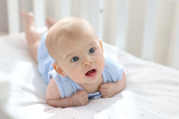 Cute little baby lying in crib at home, space for text