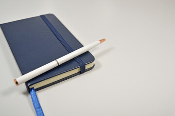 Isolated small blue notebook with a white pen placed on the left side of a white background with blank space on the right.