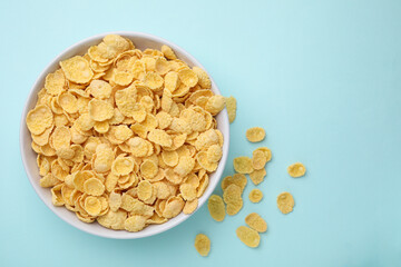 Breakfast cereal. Tasty corn flakes in bowl on light blue table, top view. Space for text