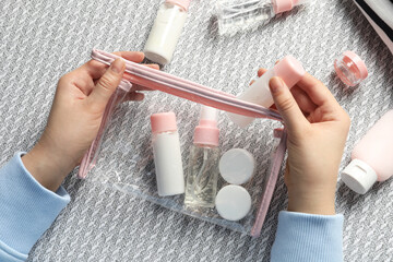 Cosmetic travel kit. Woman putting small bottle with personal care product into plastic bag on sofa, top view