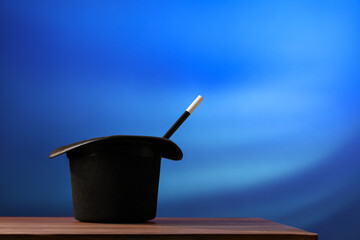 Magician's hat and wand on wooden table against blue background, space for text