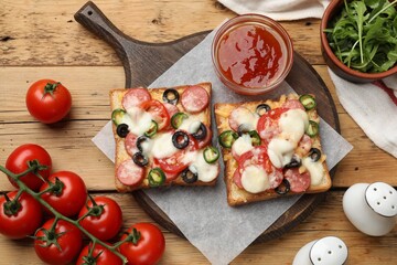 Tasty pizza toasts, sauce, arugula and tomatoes on wooden table, flat lay