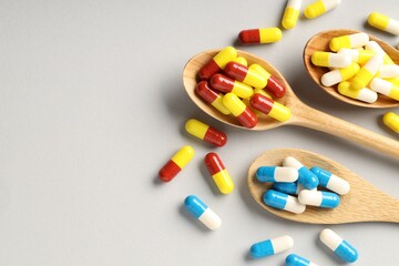 Many antibiotic pills with wooden spoons and space for text on grey background, top view. Medicinal...