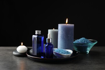 Spa composition. Cosmetic products, burning candles and sea salt on gray table against black background