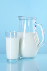 Jug and glass of fresh milk on light blue background