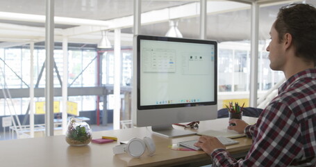Image of caucasian male colleague, wearing plaid shirt, studying large screen