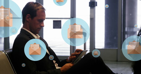 Image of message icons floating over caucasian businessman using digital tablet at an airport