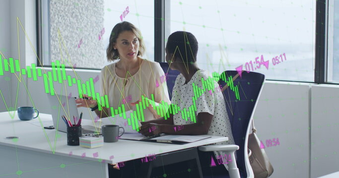 Image of multiple graphs with changing numbers, diverse female coworkers discussing on desk