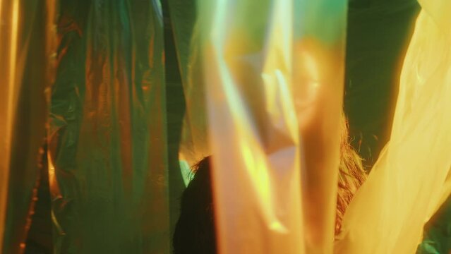 Young beautiful Asian woman walking through cellophane curtains in dark room with colorful neon light and looking around in amazement