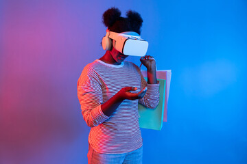 Enjoy shopping young African wearing VR looking metaverse online while holding shopping bag on...