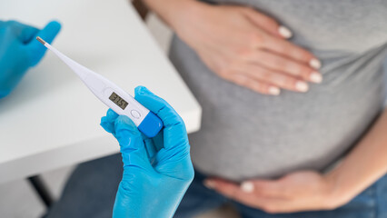 Pregnant woman with fever at doctor's appointment. Therapist holds an electronic thermometer with a...