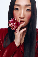 Mysterious woman with long black hair and red jacket holding flower in front of face