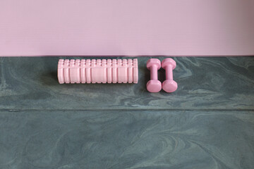 pink fitness equipment, dumbbells, self-massage roller, exercise mat on stone floor in gym, top view
