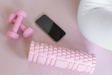 smart phone with blank screen on pink fitness background, dumbbells near female leg in white leggings