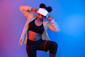 Young African sport woman wearing VR stretching whole body posing on blue neon lighting vibrant...