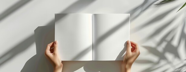 A woman's hands open an empty white book mockup on a light grey background, in a flat lay with shadows from a window, in the style of a modern minimalist. A4 format for presentation of magazine