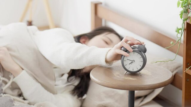 目覚ましを止め起きる女性