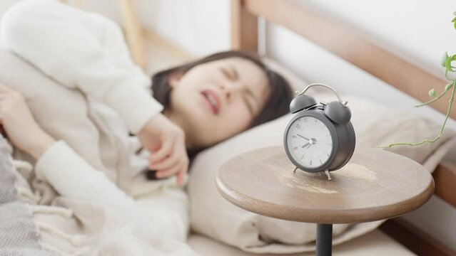 目覚ましを止め二度寝をする女性