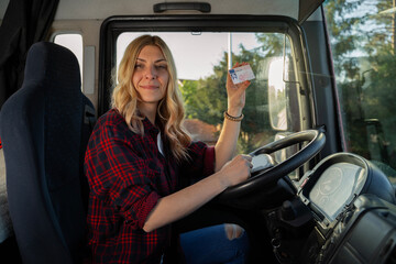 Happy charismatic woman truck driver sitting behind the steering wheel and showing her driving...
