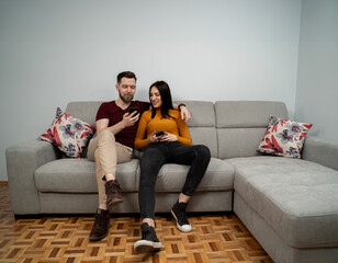 Happy young couple sitting on the couch hugged , looking both on smartphone screen 