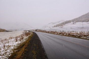 Asphalt road going through the mountain valley covered with the first snow.