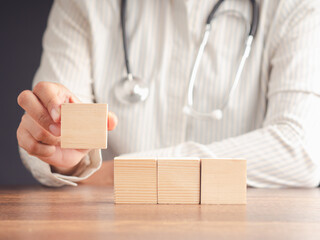 Close-up of doctor's hand holding a wooden cube on a wooden table.