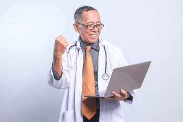Cheerful Senior Doctor Male Looking At Laptop Clenching Fist Showing Success, Winning Gesture...