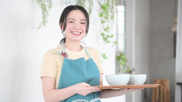 カフェで配膳するエプロン姿の接客業の女性か主婦のイメージ　いらっしゃいませの動画