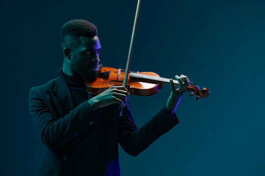 Man in suit playing violin in dramatic lighting against dark background creating a captivating musical performance atmosphere
