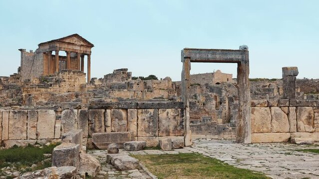 Scenic view of remnants of ancient Roman settlement of Dougga overlooking historic gate of Dar Lacheb and Capitol Temple ruins in backdrop under cloudy spring sky, Tunisia