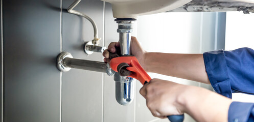 Plumber uses wrench to repair water pipe under sink There is maintenance to fix the water leak in the bathroom.with red wrench, plumbing install concept.