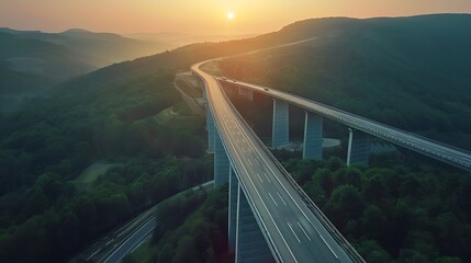 Aerial view of highway road bridge for vehicular transport as part of infrastructure development built over valley with green forest trees and hills connecting towns during sunset