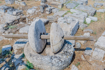 Weathered millstone at an archeological site showing ancient ruins and historical tools, in...
