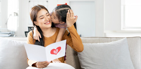 Cheerful asian mother and little daughter reading handmade greeting card with heart while  celebration mothers day at home