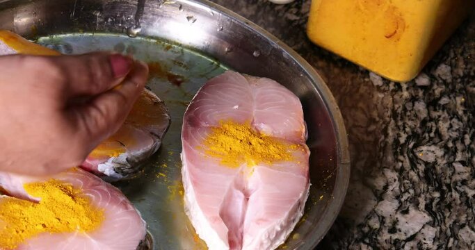 Preparing hilsa fish cut pieces for Asian Bengali cooking frying rubbing messaging marinate with salt yellow turmeric cumin spice