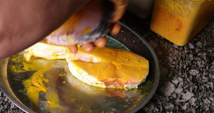 Preparing hilsa fish cut pieces for Asian Bengali cooking frying rubbing messaging marinate with salt yellow turmeric cumin spice