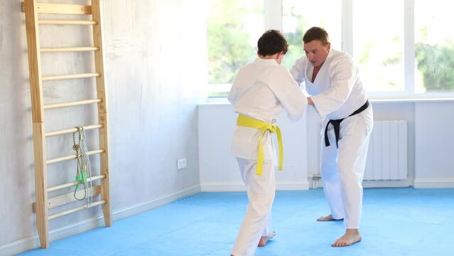 Active teen male jujutsu practitioner training battling methods with middle-aged partner in sports hall