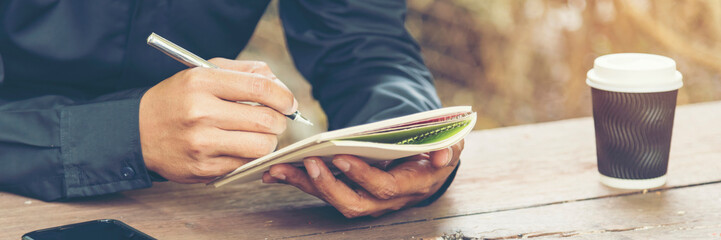 Man hands writing notebook diary with coffee cup and smartphone on wood desk. Close up man hands...