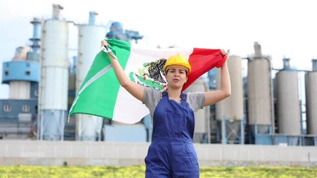 Worried girl in work clothes and hardhat with flag of mexico standing in front of industrial scenery