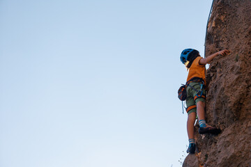 Obraz premium A determined and strong boy climber climbs a steep mountain wall. Extreme sports and rock climbing.
