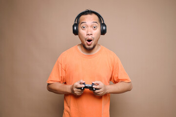 Asian gamer man playing video games using joystick with a surprise face, feeling afraid and excited 