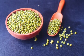 Green beans or (Vigna radiata) in a wooden bowl and some scattered on the bottom, dark background.
