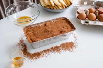 tiramisu making process. Italian dessert in foil tray and ingredients on kitchen table