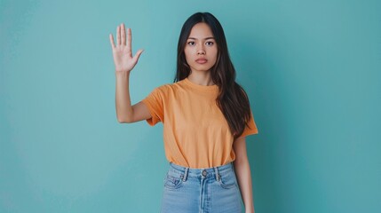 portrait of a beautiful young asian woman showing stop gesture on blue background. raise awareness,