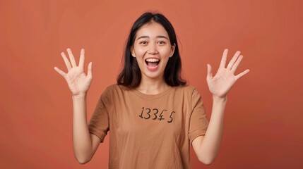 Excited young Asian woman with her hands up on a brown background.