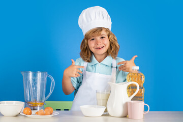 Child wearing cooker uniform and chef hat preparing vegetables on kitchen, studio portrait....
