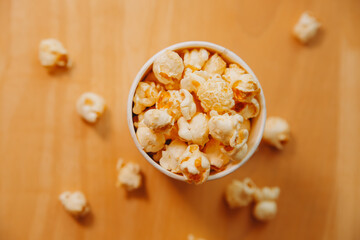 A bucket of popcorn, top-view, warm colors, light brown wooden background, flat lay, daylight macro close-up