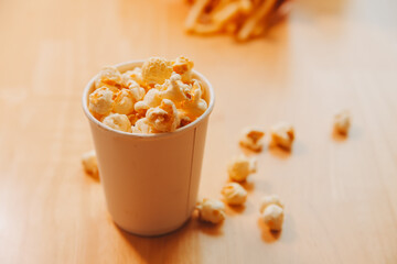 A bucket of popcorn, top-view, warm colors, light brown wooden background, flat lay, daylight macro close-up